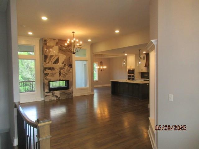 7031 N London Ave, Kansas City, MO 64151 - unfurnished living room featuring a chandelier, dark wood finished floors, recessed lighting, a stone fireplace, and baseboards