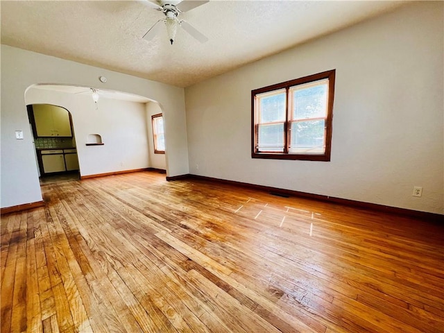 211 W 22nd St, Higginsville, MO 64037 - spare room featuring light wood-style flooring, a ceiling fan, arched walkways, baseboards, and a textured ceiling