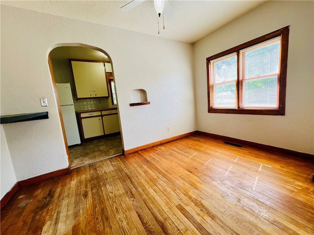 211 W 22nd St, Higginsville, MO 64037 - empty room featuring light wood finished floors, a ceiling fan, arched walkways, and baseboards