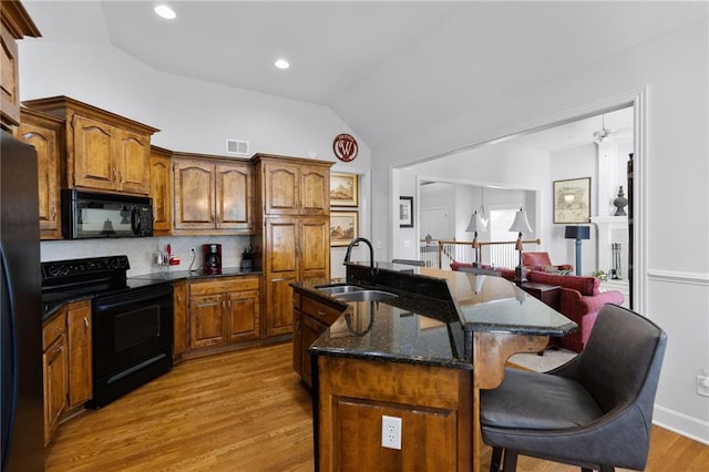 11518 W 143rd Ter, Olathe, KS 66062 - kitchen with black appliances, lofted ceiling, a kitchen bar, light wood-style floors, and a center island with sink