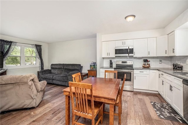 504 W 5th Ct, Peculiar, MO 64078 - kitchen featuring appliances with stainless steel finishes, open floor plan, wood finished floors, and backsplash