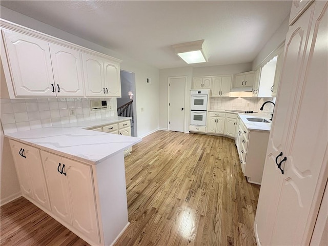 3647 NW Blue Jacket Dr, Lees Summit, MO 64064 - kitchen with white double oven, a peninsula, light wood-style floors, decorative backsplash, and white cabinets