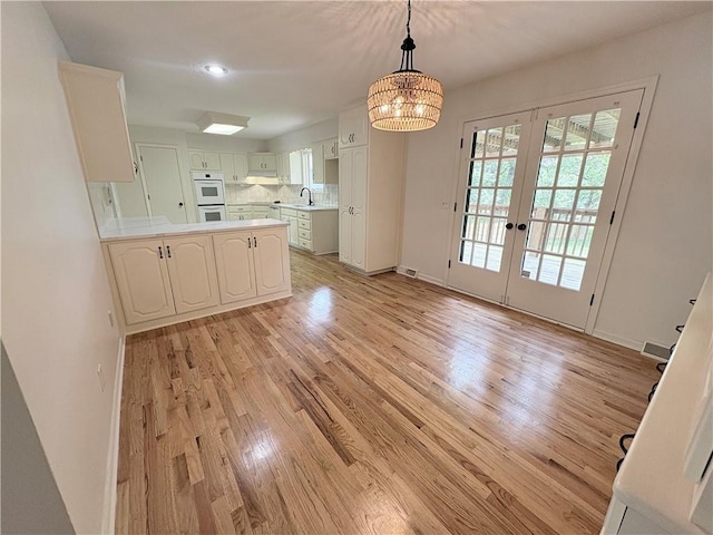 3647 NW Blue Jacket Dr, Lees Summit, MO 64064 - kitchen with a peninsula, light wood finished floors, french doors, a chandelier, and light countertops