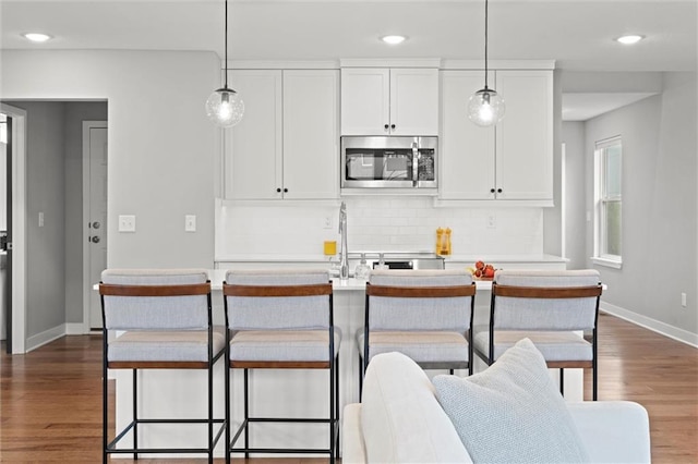 8810 SW 9th Ter, Blue Springs, MO 64064 - kitchen with stainless steel microwave, backsplash, dark wood-style floors, white cabinetry, and hanging light fixtures