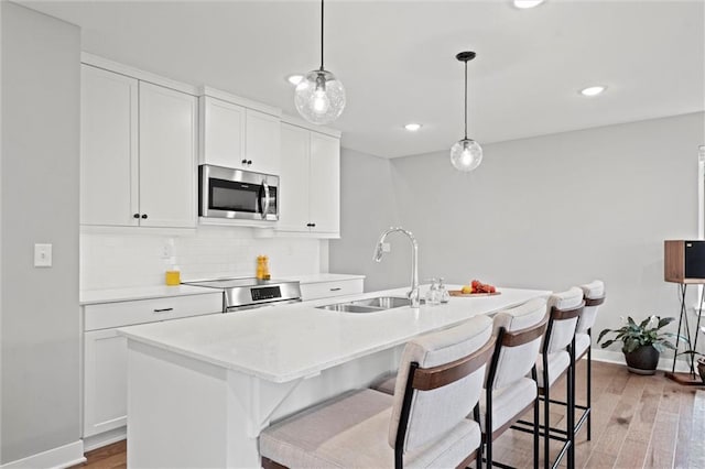 8810 SW 9th Ter, Blue Springs, MO 64064 - kitchen with stainless steel microwave, range, decorative backsplash, an island with sink, and light wood-style floors