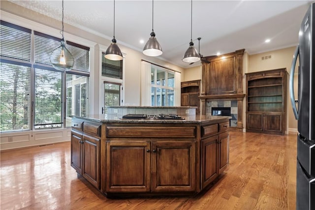 15027 Ash St, Leawood, KS 66224 - kitchen featuring freestanding refrigerator, gas cooktop, a tile fireplace, dark stone counters, and crown molding