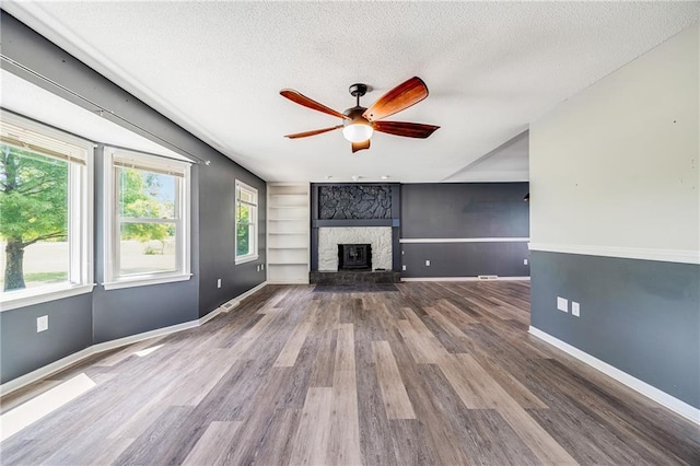 160 SW 131st Hwy, Holden, MO 64040 - unfurnished living room featuring ceiling fan, wood finished floors, a textured ceiling, a stone fireplace, and built in shelves