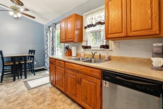 1203 S Skyline Dr, Liberty, MO 64068 - kitchen featuring stainless steel dishwasher, a ceiling fan, vaulted ceiling, brown cabinets, and light countertops
