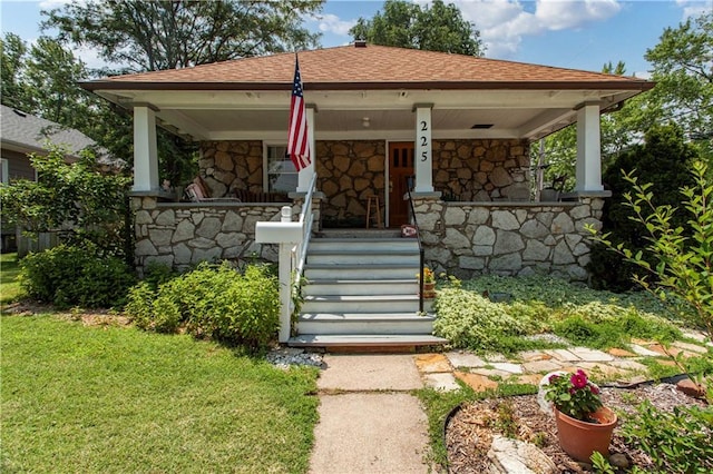 225 W Moore St, Independence, MO 64050 - view of front of home featuring stone siding, covered porch, a shingled roof, and a front yard