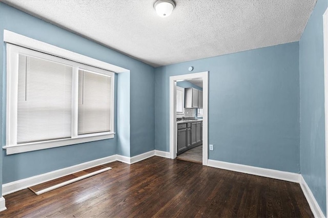 5701 Wabash Ave, Kansas City, MO 64130 - spare room with dark wood finished floors, baseboards, a sink, and a textured ceiling
