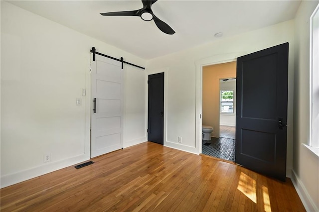 1220 E 24th Ave, Kansas City, MO 64116 - unfurnished bedroom with a barn door, hardwood / wood-style flooring, baseboards, and a ceiling fan