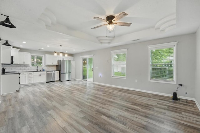 503 N Washington St, East Lynne, MO 64743 - unfurnished living room featuring a sink, baseboards, ceiling fan, light wood finished floors, and a raised ceiling