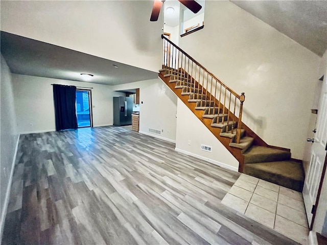 766 Spring Cir, Liberty, MO 64068 - unfurnished living room featuring stairway, wood finished floors, baseboards, a ceiling fan, and a towering ceiling