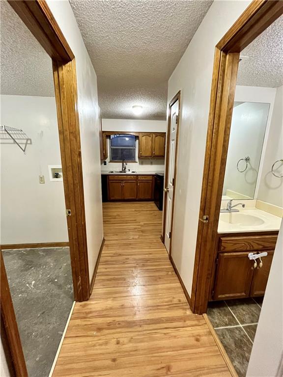 766 Spring Cir, Liberty, MO 64068 - hallway with a textured ceiling, a sink, and light wood-style floors