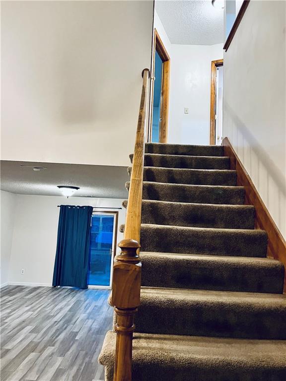 766 Spring Cir, Liberty, MO 64068 - staircase with wood finished floors, a textured ceiling, and baseboards