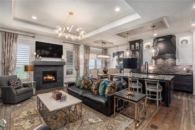 15278 W 173rd St, Olathe, KS 66062 - living area featuring dark wood-type flooring, a tray ceiling, a warm lit fireplace, a chandelier, and recessed lighting