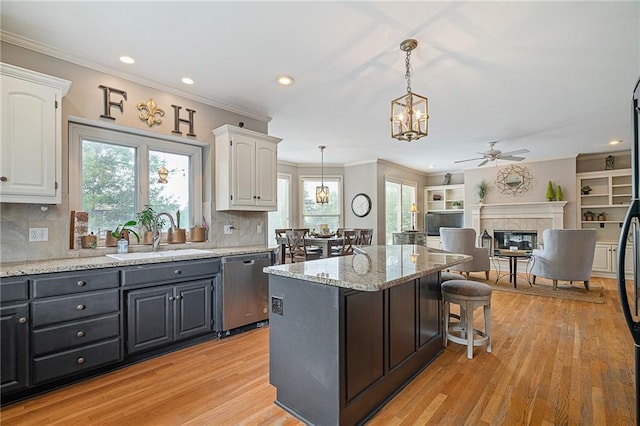 15998 Overbrook Ln, Overland Park, KS 66224 - kitchen featuring dishwasher, ceiling fan, white cabinetry, a tiled fireplace, and a kitchen bar