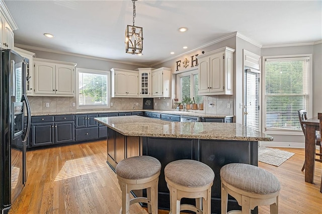 15998 Overbrook Ln, Overland Park, KS 66224 - kitchen featuring black refrigerator with ice dispenser, a kitchen breakfast bar, light wood-type flooring, white cabinetry, and crown molding