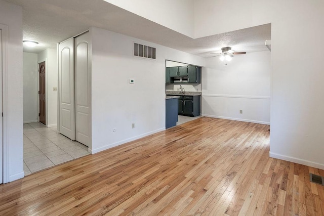 255 N Michigan St Unit 1-2, Lawrence, KS 66044 - unfurnished living room featuring a ceiling fan, light wood finished floors, a sink, a textured ceiling, and baseboards
