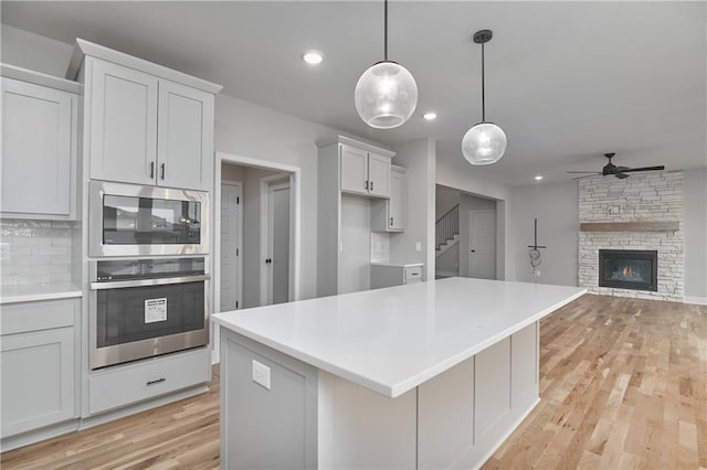 6018 Arapahoe St, Shawnee, KS 66226 - kitchen with appliances with stainless steel finishes, ceiling fan, light wood-style floors, a stone fireplace, and a center island