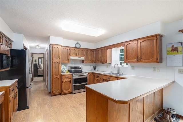 307 E Gore Rd, Raymore, MO 64083 - kitchen featuring appliances with stainless steel finishes, a sink, a peninsula, light wood-style flooring, and brown cabinetry