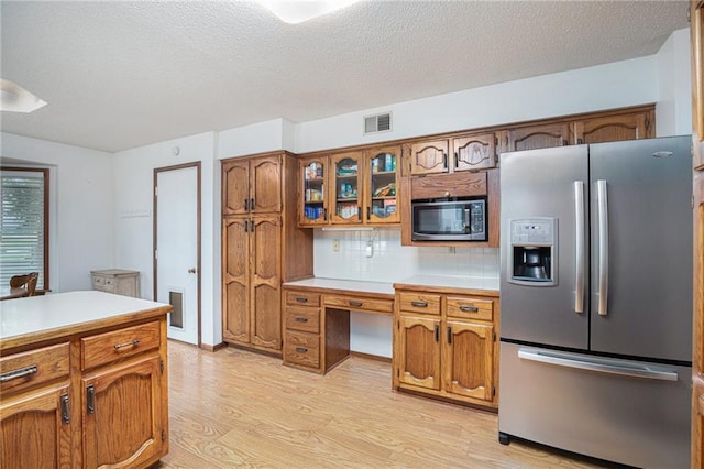 307 E Gore Rd, Raymore, MO 64083 - kitchen with stainless steel appliances, light wood-type flooring, light countertops, brown cabinets, and a textured ceiling