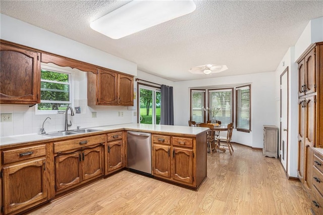 307 E Gore Rd, Raymore, MO 64083 - kitchen featuring stainless steel dishwasher, a sink, a textured ceiling, a peninsula, and light wood-style floors