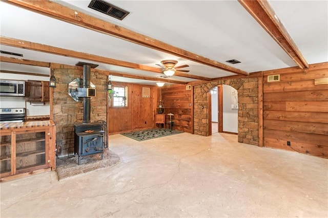 5470 SE Downing Rd, Lathrop, MO 64465 - unfurnished living room with wood walls, beam ceiling, concrete flooring, arched walkways, and a wood stove