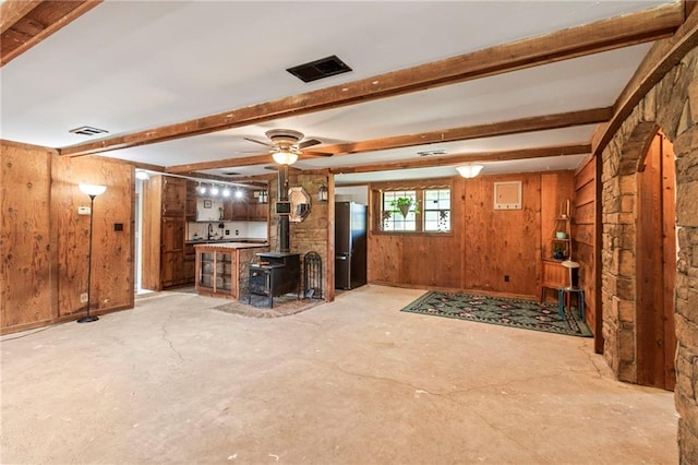 5470 SE Downing Rd, Lathrop, MO 64465 - unfurnished living room featuring a wood stove, wooden walls, beamed ceiling, a ceiling fan, and concrete floors