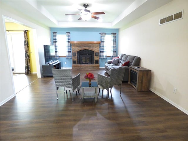 520 N Jefferson St, Raymore, MO 64030 - living room featuring a tray ceiling, a ceiling fan, a brick fireplace, wood finished floors, and baseboards