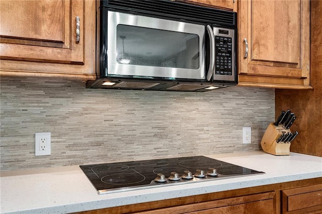 8709 Pine St, Lenexa, KS 66220 - kitchen with stainless steel microwave, black electric cooktop, brown cabinets, and backsplash