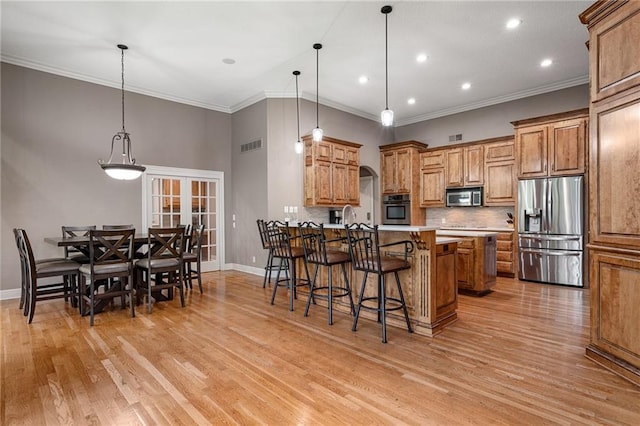 8709 Pine St, Lenexa, KS 66220 - kitchen featuring appliances with stainless steel finishes, brown cabinetry, a kitchen bar, tasteful backsplash, and light wood-style flooring