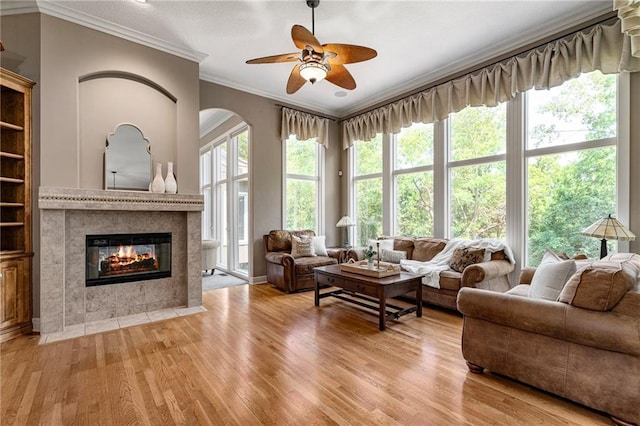 8709 Pine St, Lenexa, KS 66220 - living room featuring crown molding, light wood finished floors, a ceiling fan, a tiled fireplace, and arched walkways