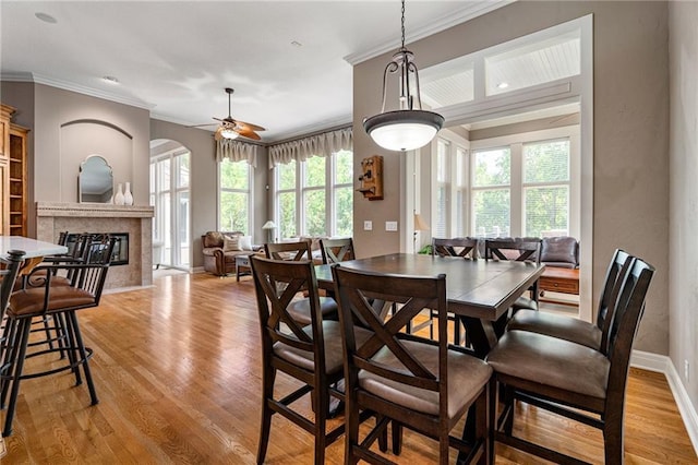 8709 Pine St, Lenexa, KS 66220 - dining area featuring ornamental molding, light wood-style floors, a fireplace, a ceiling fan, and arched walkways