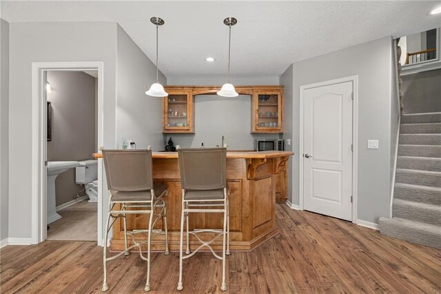 8709 Pine St, Lenexa, KS 66220 - kitchen with brown cabinetry, a kitchen bar, wood finished floors, glass insert cabinets, and recessed lighting