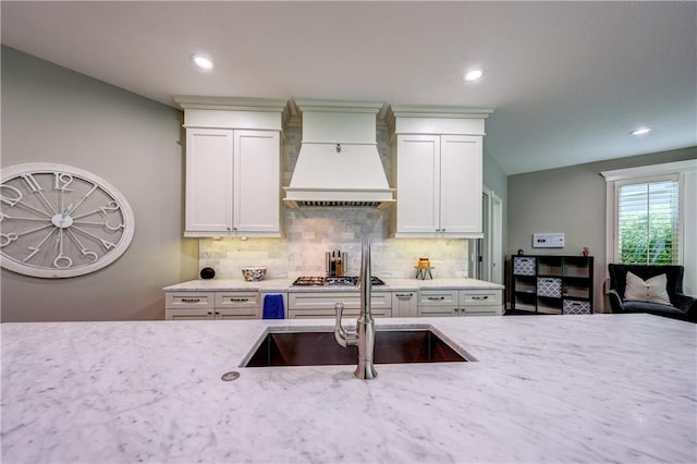 14911 Outlook Ln, Overland Park, KS 66223 - kitchen with premium range hood, tasteful backsplash, stainless steel gas cooktop, white cabinets, and light stone counters