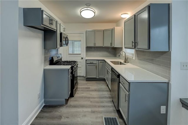 6117 Harrison St, Kansas City, MO 64110 - kitchen featuring appliances with stainless steel finishes, a sink, light wood finished floors, and gray cabinetry