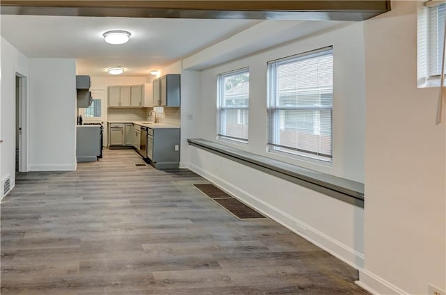 6117 Harrison St, Kansas City, MO 64110 - kitchen with gray cabinetry, stainless steel dishwasher, light countertops, wood finished floors, and baseboards