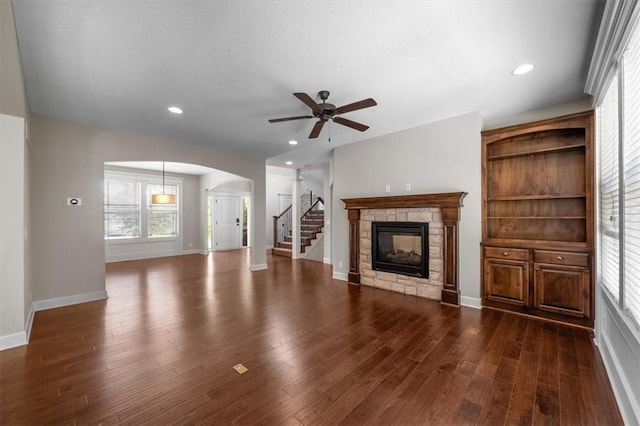 9154 Shady Bend Rd, Lenexa, KS 66227 - unfurnished living room with arched walkways, a ceiling fan, a fireplace, dark wood-style flooring, and stairs