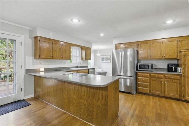 11409 Riley St, Overland Park, KS 66210 - kitchen featuring stainless steel appliances, brown cabinetry, light wood-type flooring, a peninsula, and backsplash