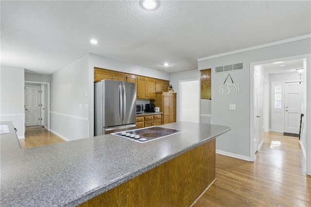 11409 Riley St, Overland Park, KS 66210 - kitchen with appliances with stainless steel finishes, brown cabinetry, a textured ceiling, wood finished floors, and a peninsula