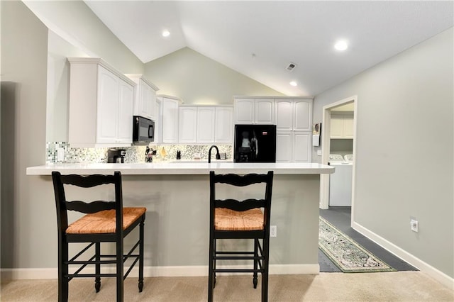 7226 Meadow View St, Shawnee, KS 66227 - kitchen with black appliances, washer and clothes dryer, a kitchen breakfast bar, vaulted ceiling, and tasteful backsplash