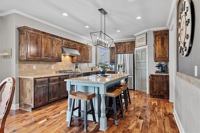17746 W 165th Pl, Olathe, KS 66062 - kitchen with under cabinet range hood, appliances with stainless steel finishes, light wood-type flooring, dark brown cabinets, and a breakfast bar