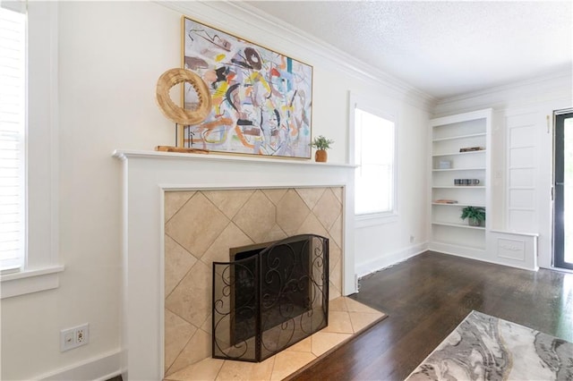 4930 Holly St, Kansas City, MO 64112 - living room featuring wood finished floors, a tiled fireplace, ornamental molding, a textured ceiling, and built in shelves