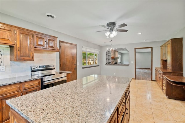 2207 N 154th Ter, Basehor, KS 66007 - kitchen with stainless steel range with electric stovetop, a center island, brown cabinetry, a ceiling fan, and light stone counters