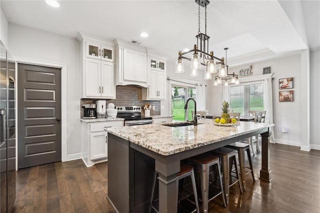1402 NW Red Oak Ct, Grain Valley, MO 64029 - kitchen with stainless steel range with electric cooktop, an island with sink, light stone countertops, a breakfast bar area, and white cabinets