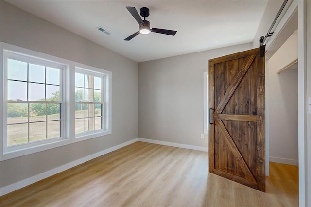 350 NW 1201st Rd, Holden, MO 64040 - unfurnished bedroom with a barn door, light wood-style flooring, and ceiling fan