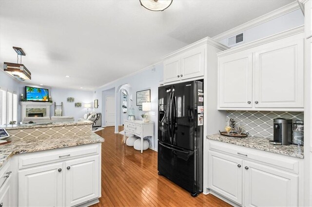 600 SW Gentry Ln, Lees Summit, MO 64081 - kitchen with black fridge, open floor plan, light wood-style floors, white cabinets, and arched walkways