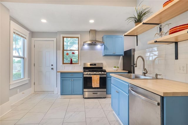 3521 Windsor Ave, Kansas City, MO 64123 - kitchen featuring blue cabinetry, appliances with stainless steel finishes, wall chimney range hood, open shelves, and light marble finish floors