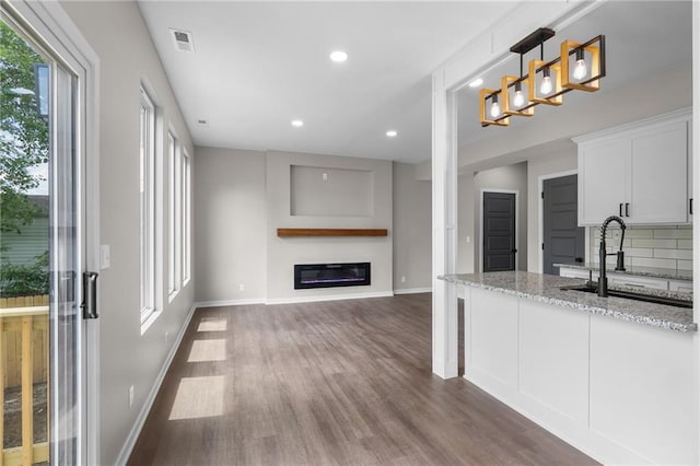 1141 Walnut Ave, Osawatomie, KS 66064 - kitchen featuring wood finished floors, light stone counters, a glass covered fireplace, white cabinets, and decorative backsplash